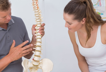 Back pain specialist showing a model of a spine to a client