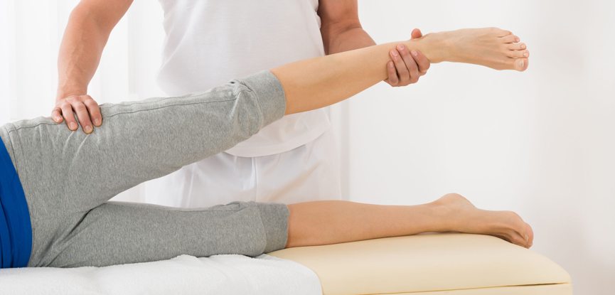 massage therapist holding client's leg while client is lying down on massage bed