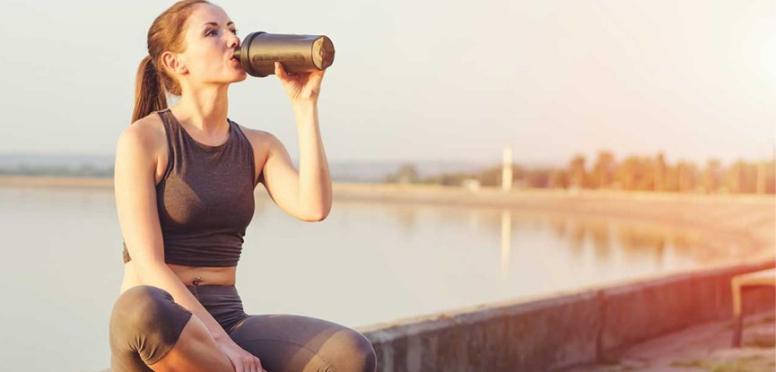 a woman sat on a wall in active wear drinking from a sports bottle