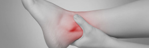 Person holding their injured ankle which is highlighted in red to show inflammation
