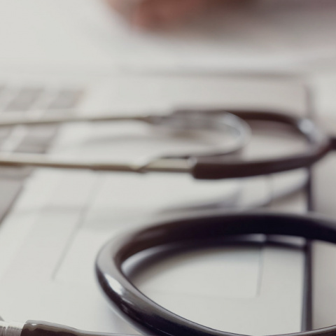 A doctor sat a desk with a MacBook and a stethoscope