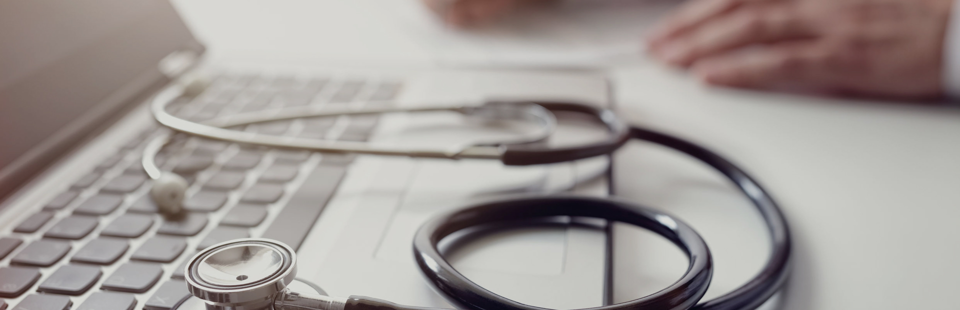 A doctor sat a desk with a MacBook and a stethoscope