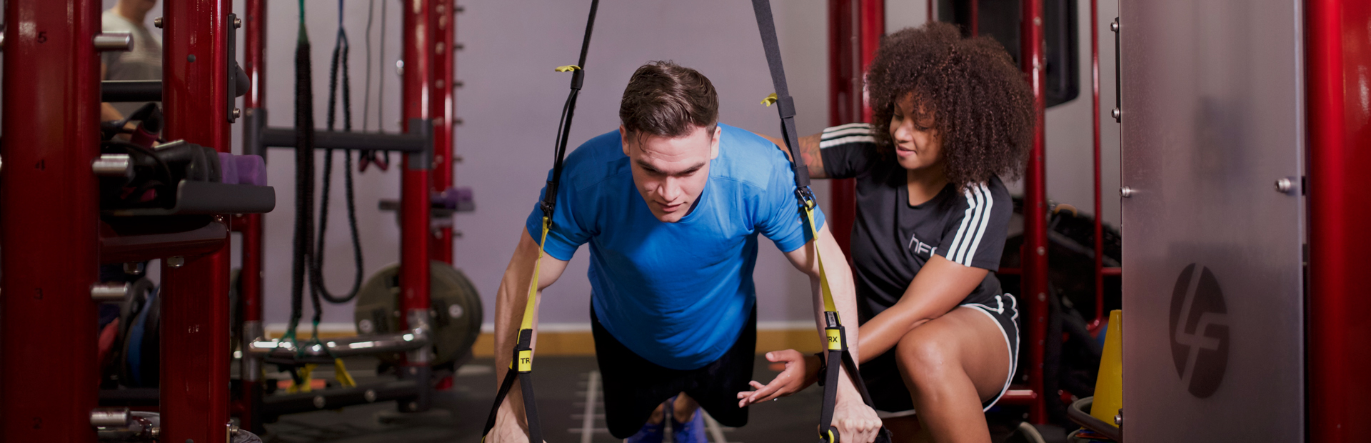A self-employed personal trainer working with a client on TRX suspension straps