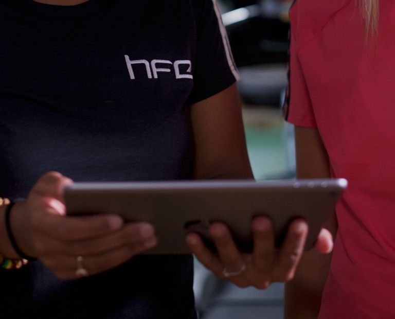 An HFE personal trainer trainer holding an iPad and talking to a student