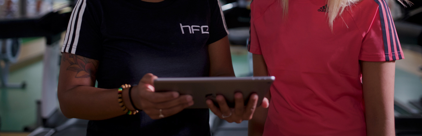 An HFE personal trainer trainer holding an iPad and talking to a student