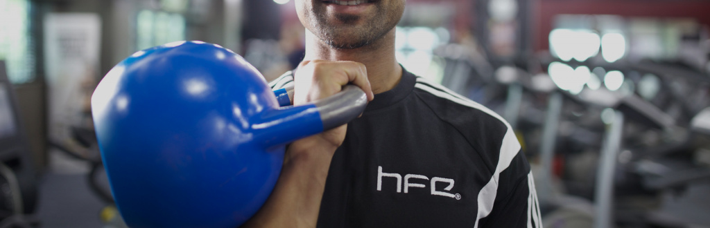 A qualified personal trainer holding a blue kettlebell