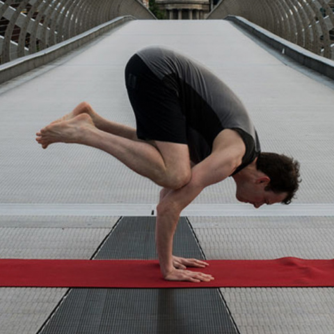 Scott Robinson, Yogibanker, performing crow pose on a bridge