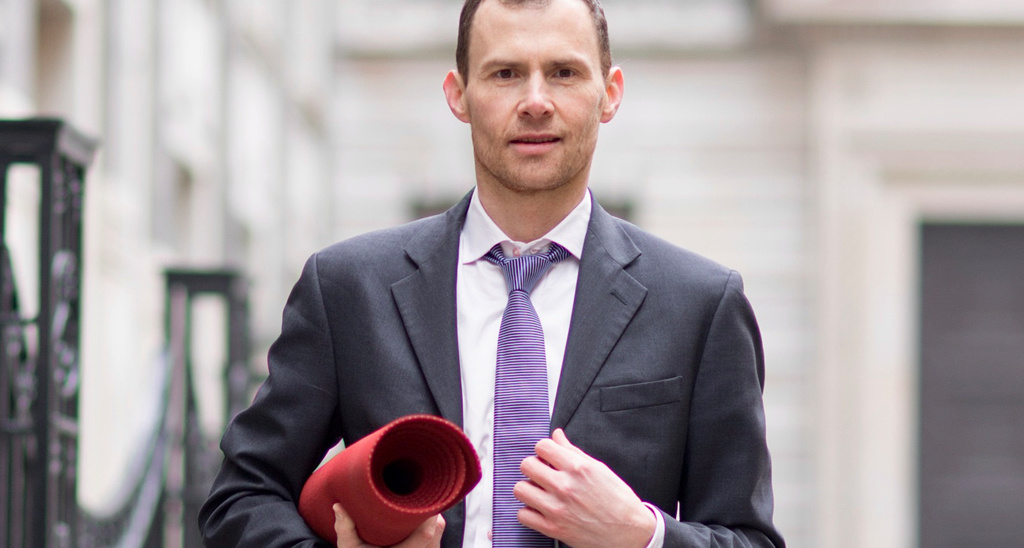 Creator of Yogibanker Scott Robinson dressed in a suit and carrying a yoga mat