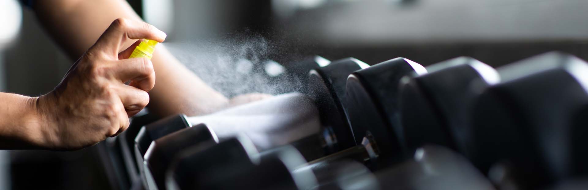 Man spraying dumbbels with sanitiser