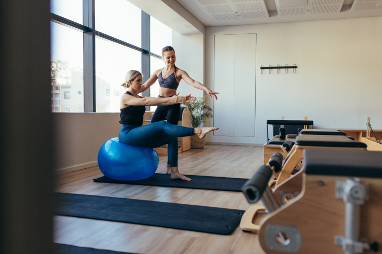 Pilates teacher assisting student with exercise ball