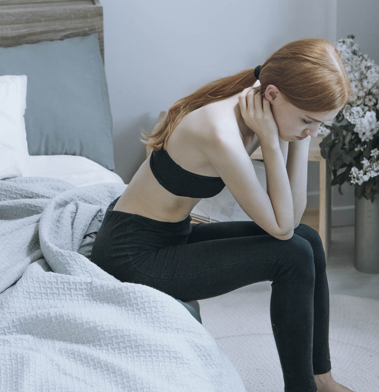 female sat on end of bed with head in hands