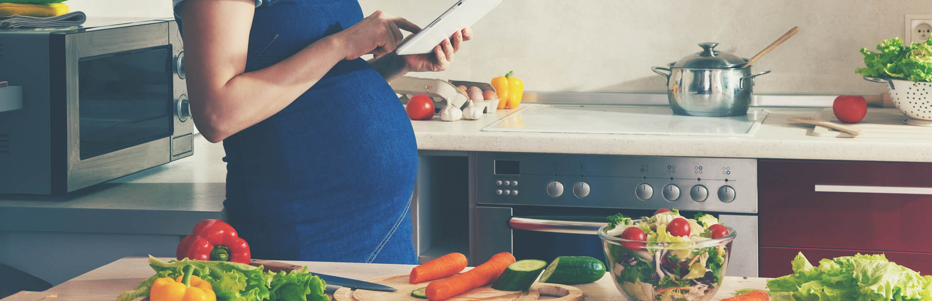 Pregnant woman at kitchen counter with various fruit and vegetables
