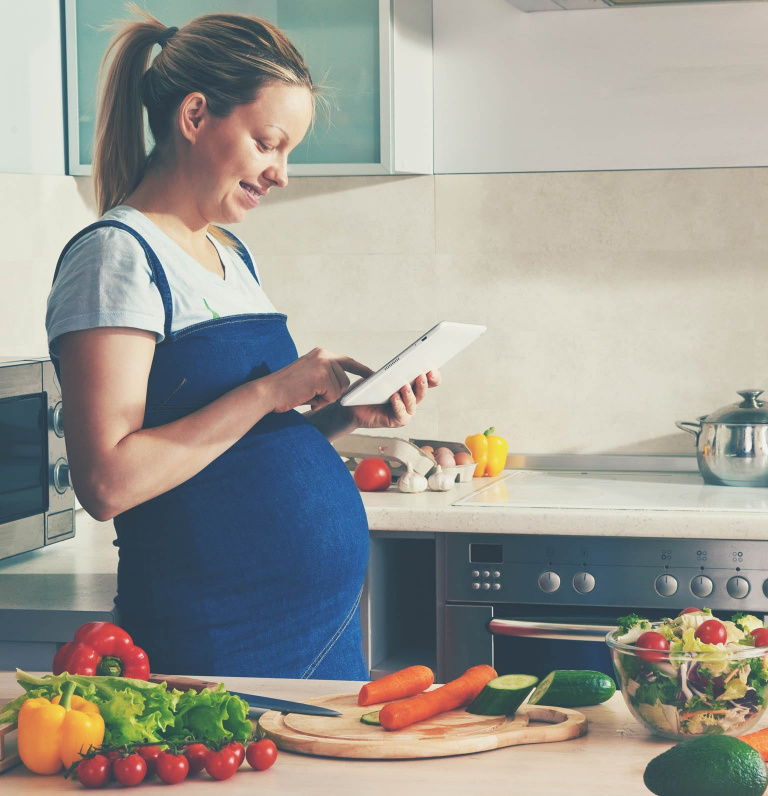 pregnant woman at kitchen counter with various fruits and vegetables