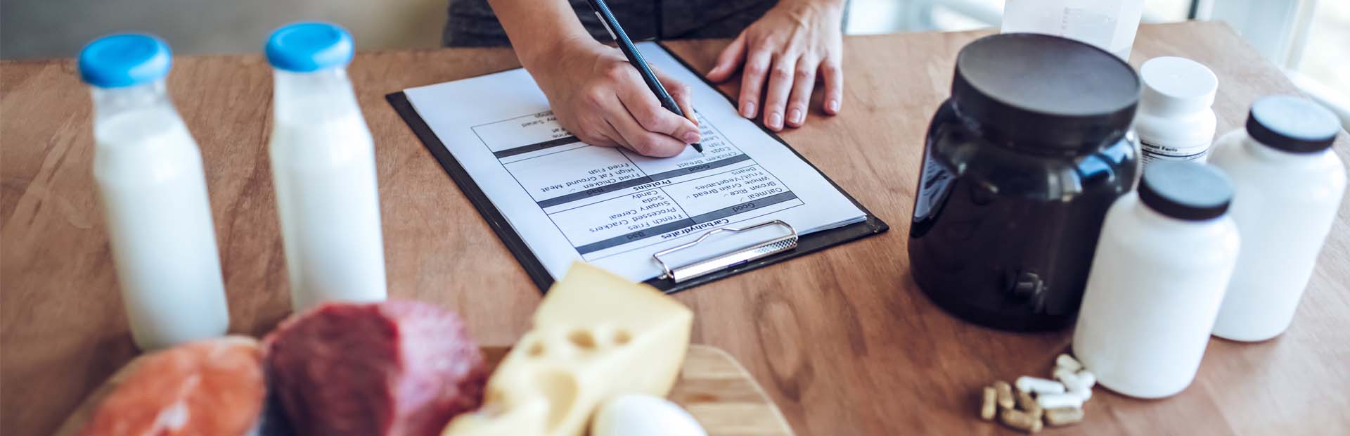 Female at table of food and supplement containers filling out food tracking on clipboard