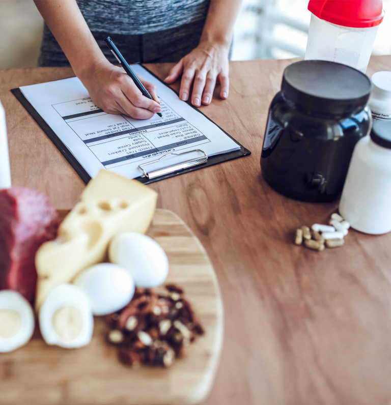 Female at table of food and supplement containers filling out food tracking on clipboard