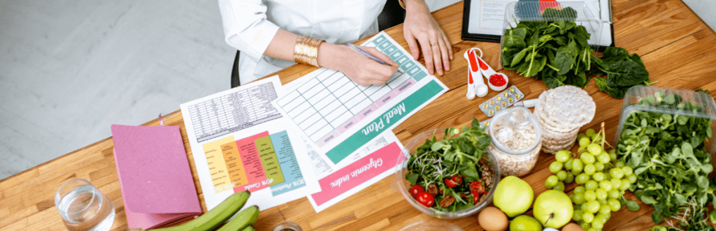 woman sat at wooden table filling out a meal plan on paper surrounded by a range of different foods