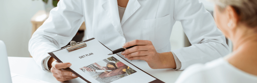 nutritionist sat with client pointing at a diet plan on a clipboard