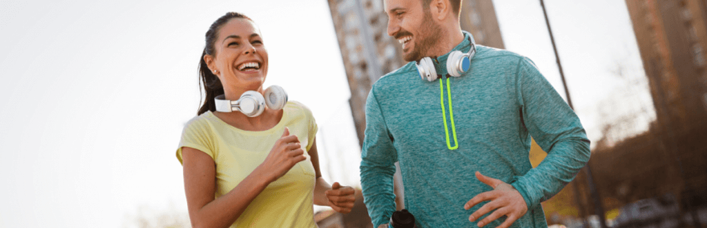 a man and woman both in active wear running together on a pavement and laughing together