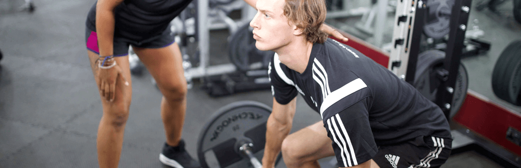 Personal trainer encouraging client while using barbell