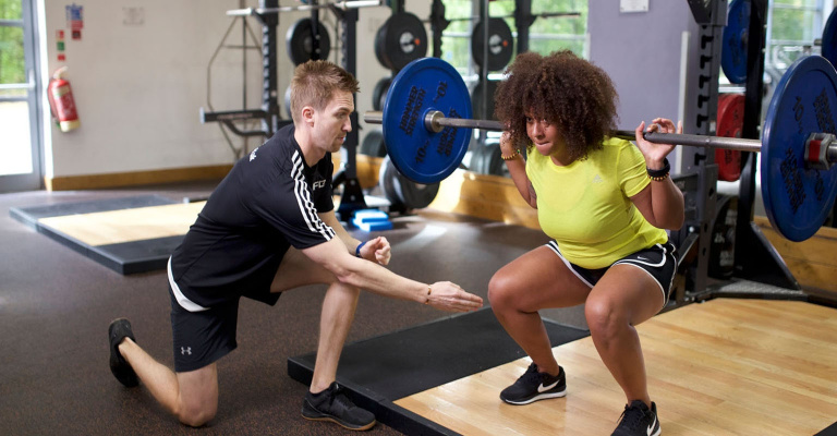Personal Trainer working with female client in the squat exercise.