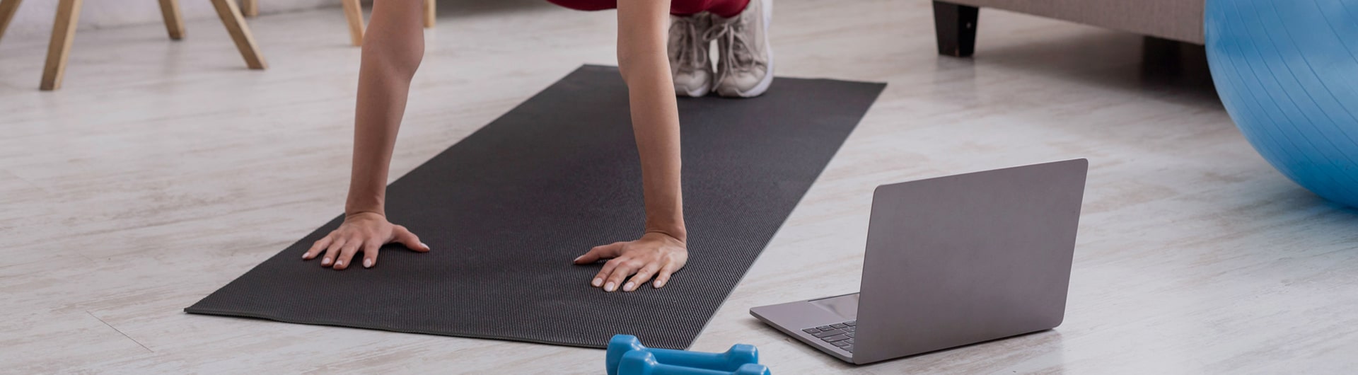 A person on a training mat with a laptop and dumbells at their side.