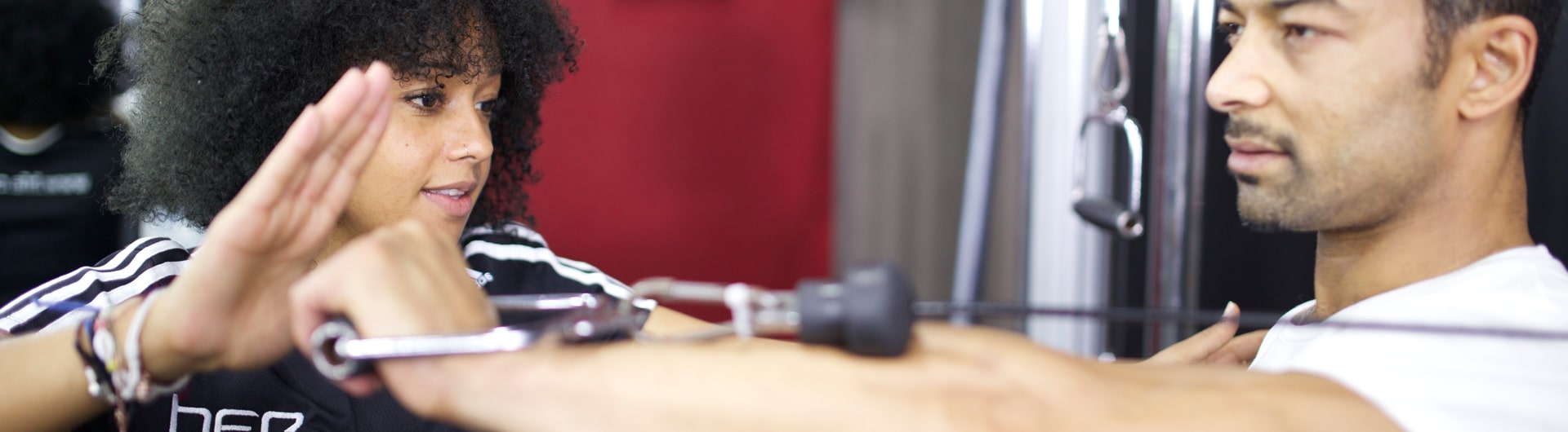 A HFE personal trainer guides a client through a cable exercise.