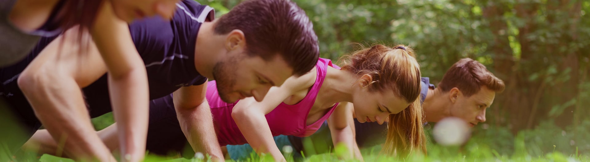 Four people engaging in a plank-type exercise on grass.