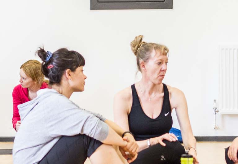 A HFE Pilates course teacher speaks to a student (left) and a circle of four students sit in discussion (right).