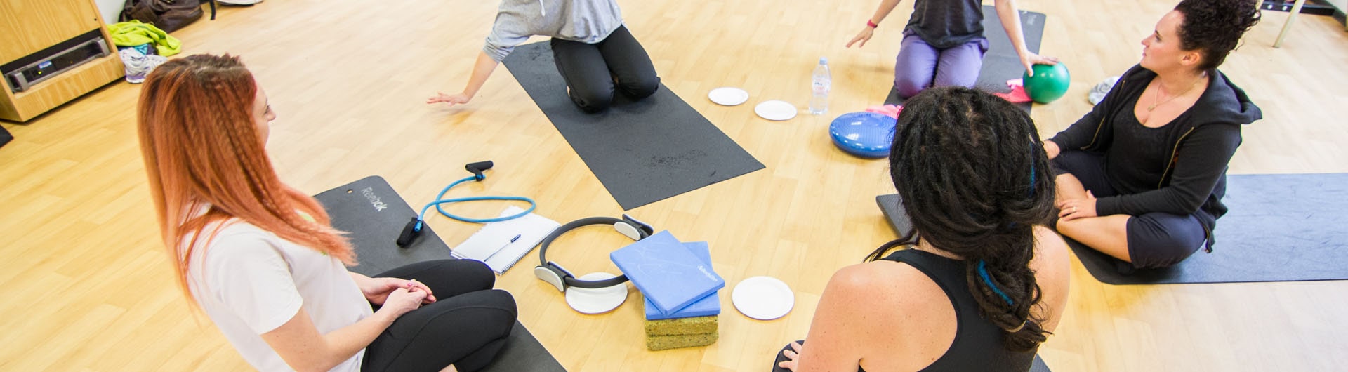 A group of HFE Pilates students discuss and take notes on an exercise.