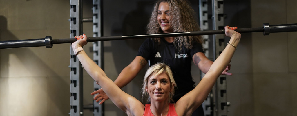 A PT guiding a client to complete an overhead press