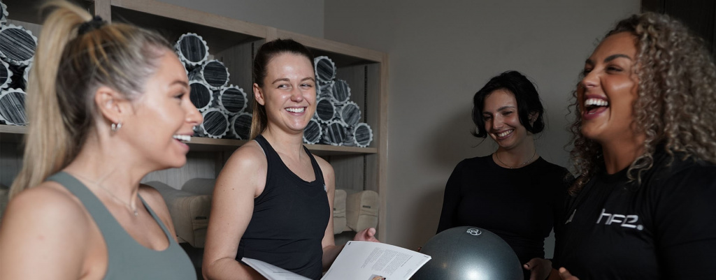A PT talking to three students in a gym setting, who are all smiling