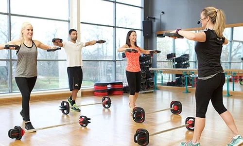 A class instructor teaching three students how to lift weights to music.