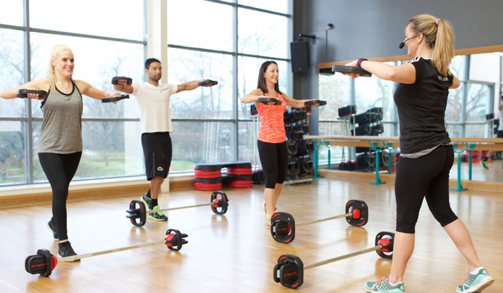 A class instructor teaching three students how to lift weights to music.