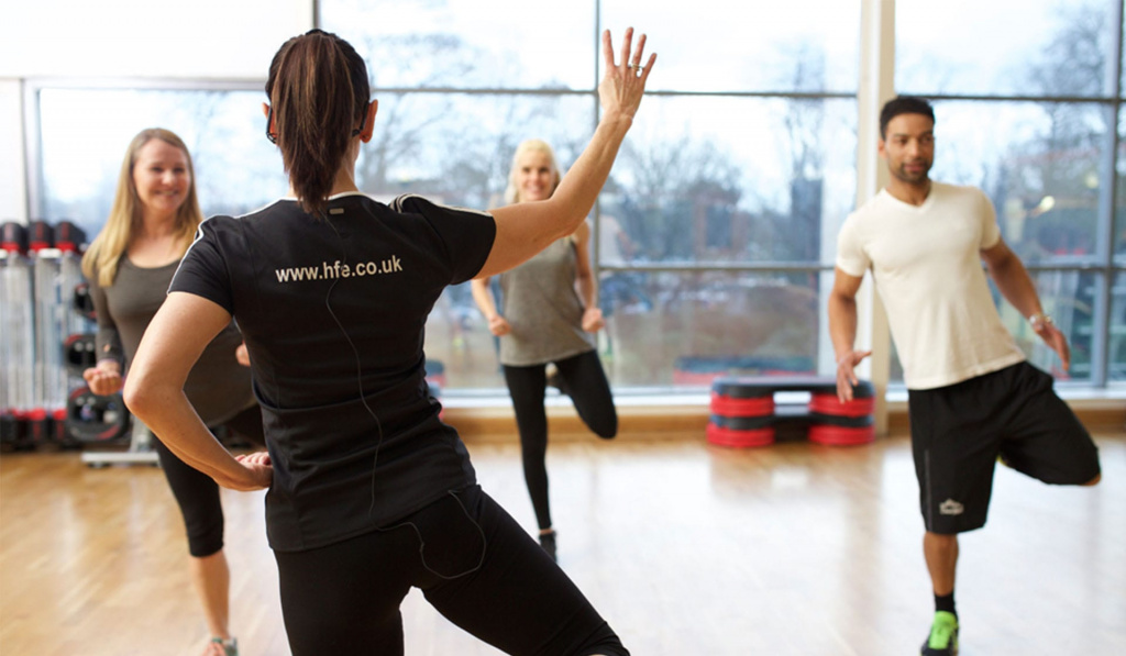 A class instructor facing away from the camera teaching three students exercises in a music exercise class