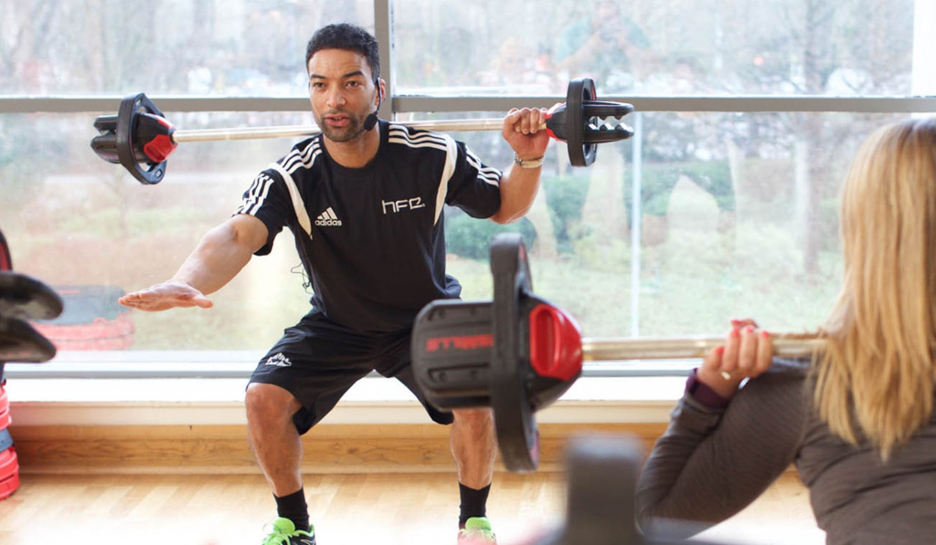 A class instructor completing a barbell squat in front of a class of students