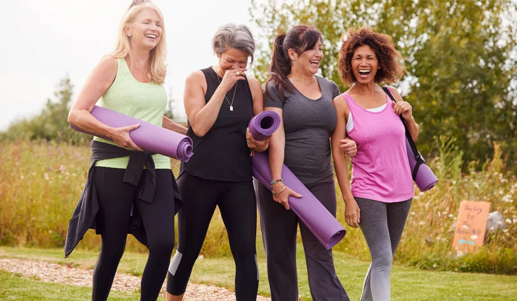 Four females walking outside together dressed in gym clothes and carrying yoga mats.