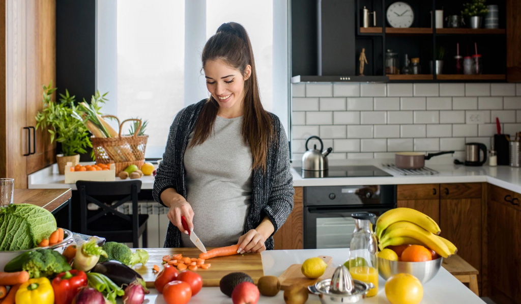 A pregnant woman in a kitchen preparing a meal.