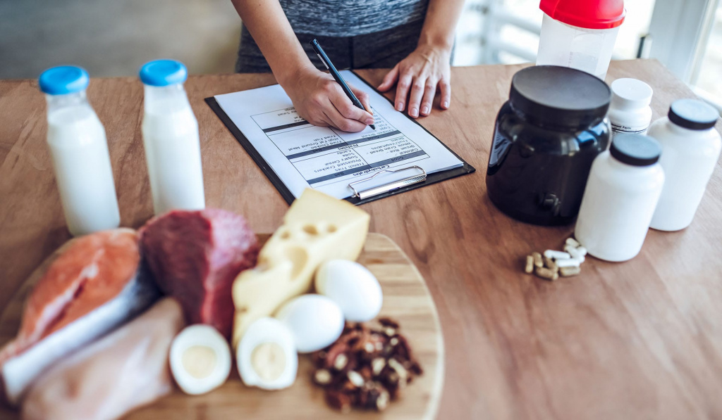 A sports nutrition coach writing a food schedule on a counter that has a variation of food and supplements.