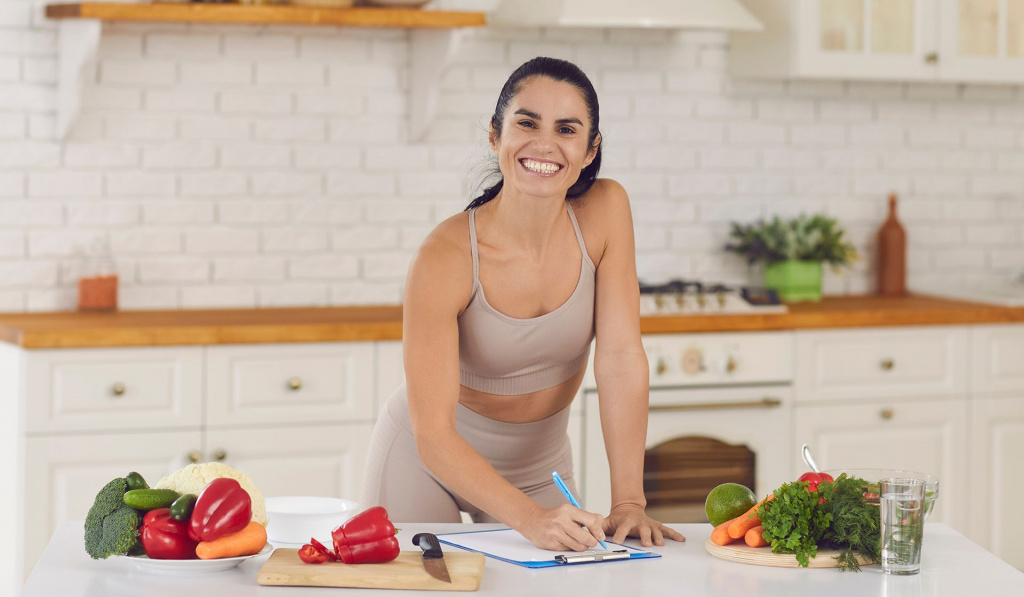 A lady in a kitchen writing a nutrition meal plan on paper and a clipboard.