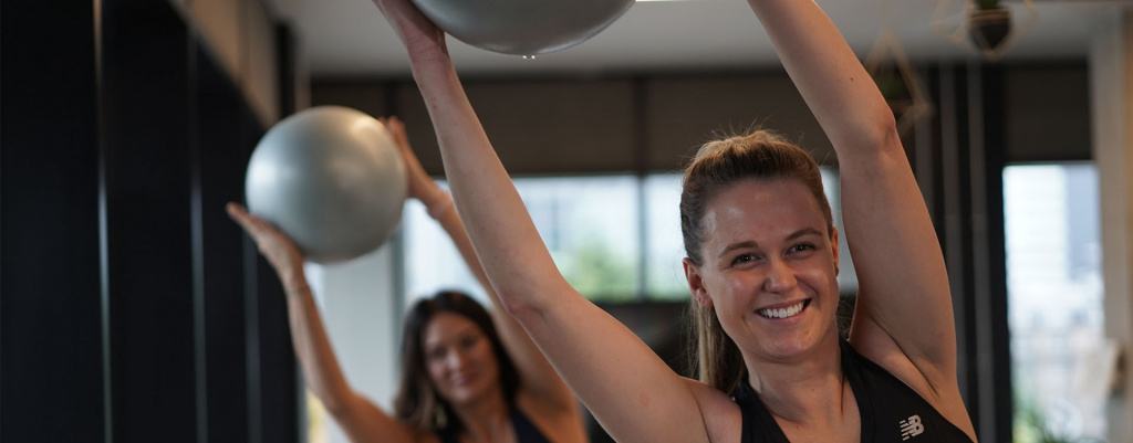 Two students in a Pilates class holding a Pilates ball over their head