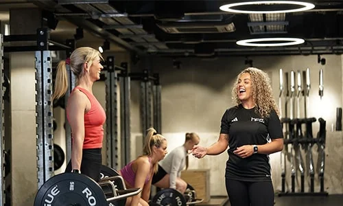 A personal trainer helping a client with a deadlift while laughing.