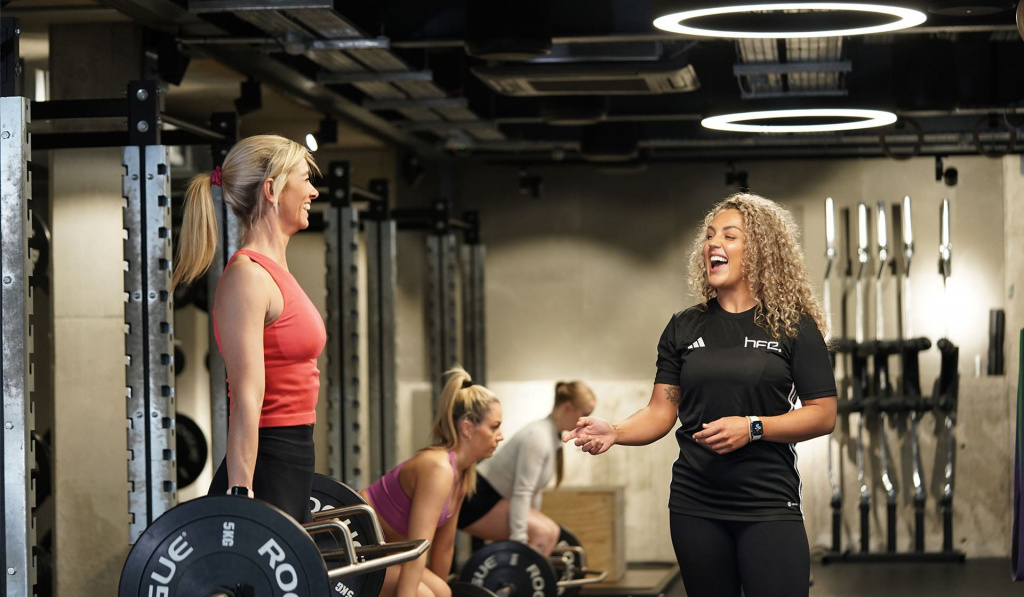 A personal trainer helping a client with a deadlift while laughing