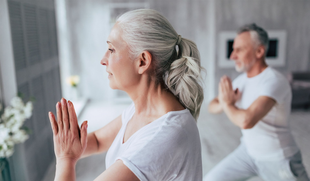 Two older adults completing a yoga pose with their hands pressed together