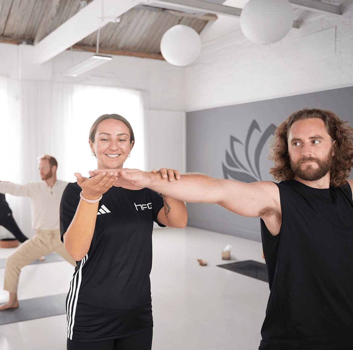 A female yoga instructor helping a male student in her class