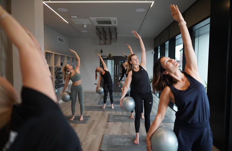 Students in a Pilates studio completing a Pilates exercise on a mat with a ball