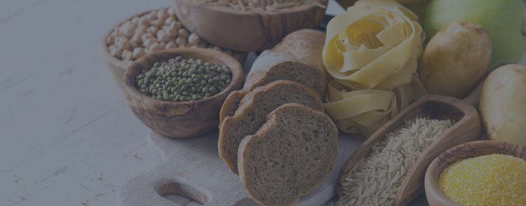 A group of carbohydrates, including potatoes, bread, pasta and rice, spread out on a table