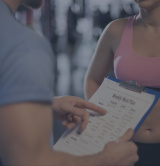 A male PT pointing to a nutrition plan on a clip board A male PT pointing to a nutrition plan on a clip board