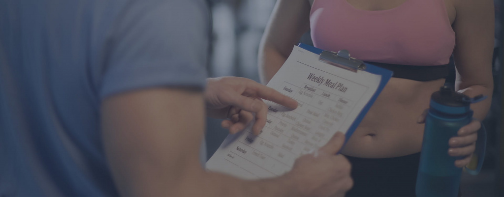 A male PT pointing to a nutrition plan on a clip board A male PT pointing to a nutrition plan on a clip board