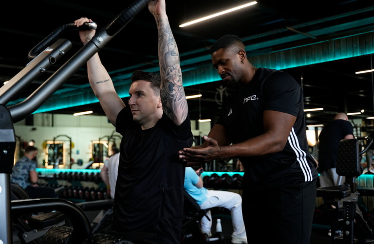 A male PT supporting a client using a machine in the gym