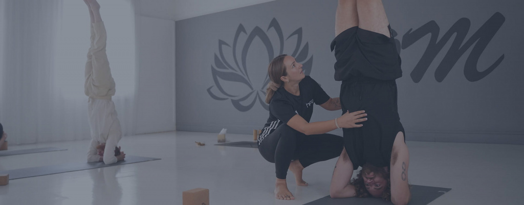 A female yoga instructor assisting a student completing a headstand pose